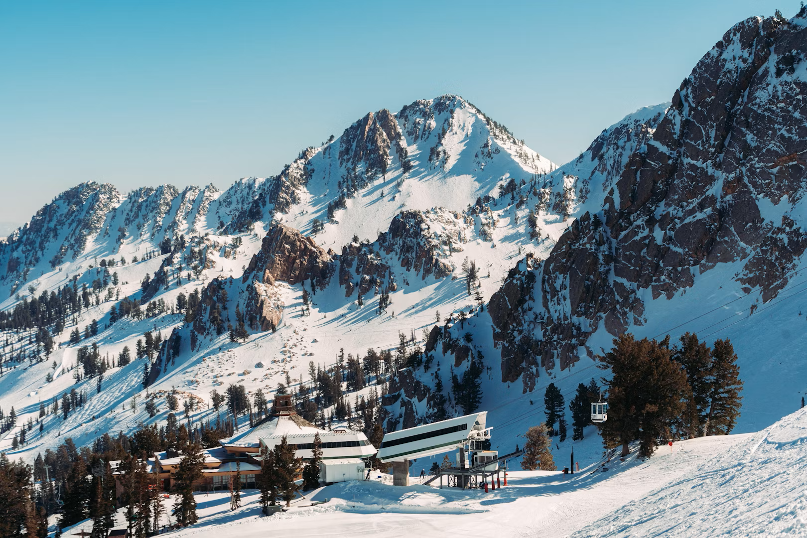 Snowbasin ski terrain with jagged snowy peaks, lift station, and bright winter sky